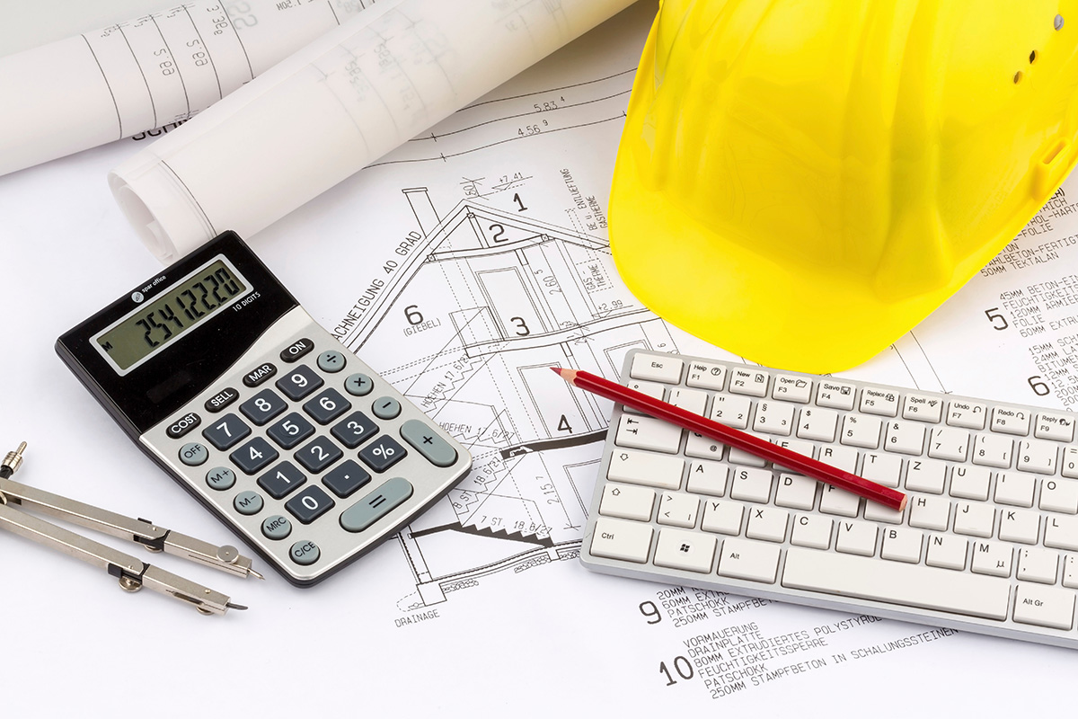 a white calculator on a desk next to a keyboard, on top of a construction blueprint and a yellow hard hat